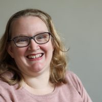 Kim Collinson Photograph of Advocate Kim Collinson, a woman with wavy, blonder, shoulder-length hair and blue eyes smiling at the camera. She is wearing thin framed glasses and a pink jumper.