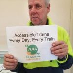 Man holding a sign saying Accessible Trains, Every Day, Every Train
