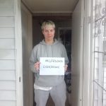 Woman with short blond hair holds a #LifelongLockdown sign on her front door
