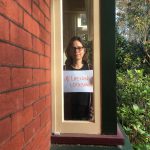 Woman standing in a window holding a #LifelongLockdown sign