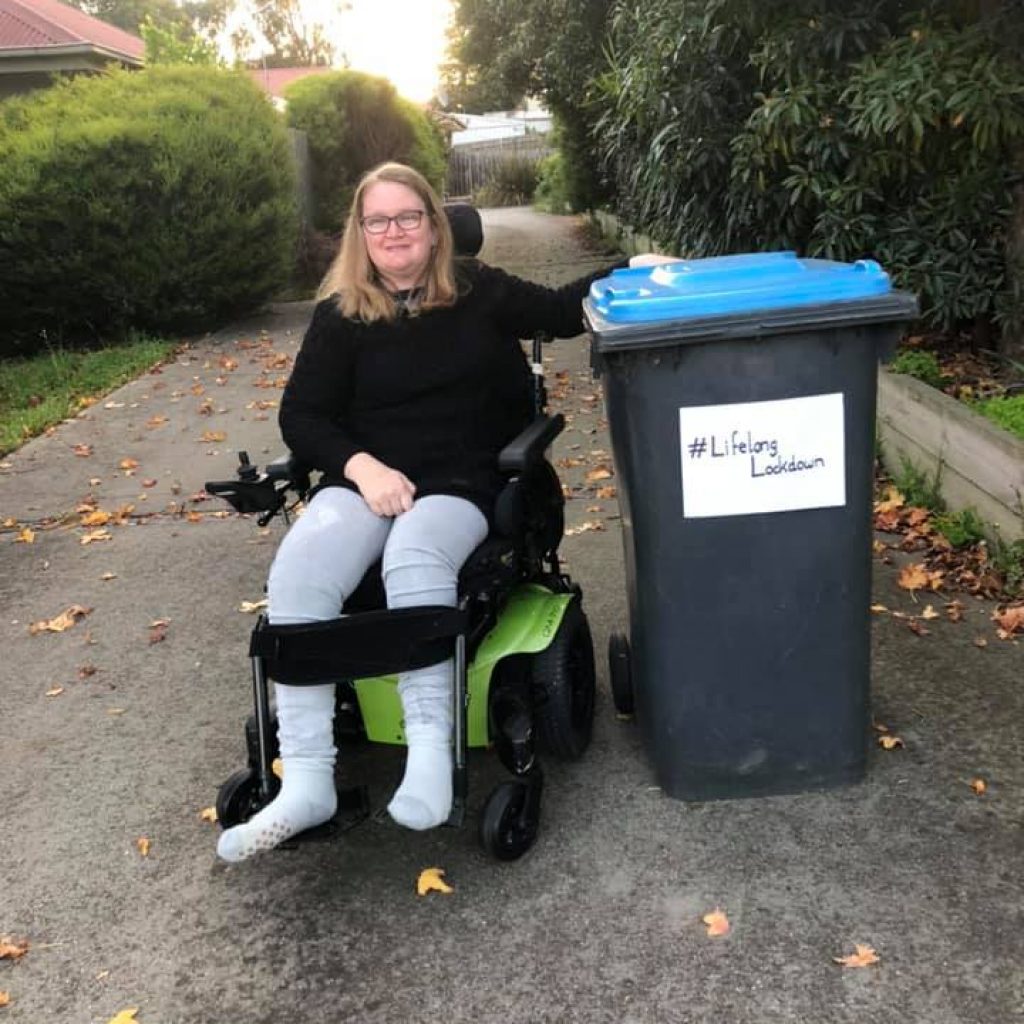 woman in a wheelchair beside a big outdoor bin. The bin has #LifelongLockdown on it