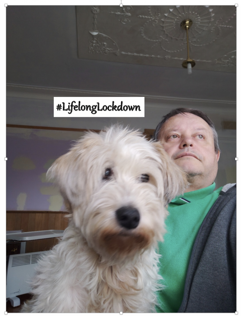 Man with very cute dog on his lap, #lifelonglockdown is written on the screen