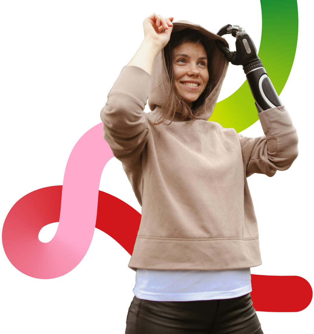 A person with a light-coloured tan hoodie, with their arms raised above their head, holding the top of the hoodie with a small smile. They have a a black prosthetic on their right hand. Behind them is a light-coloured background, and a swirl with gradients of green, pink and red that match our Disability Rights and Culture logo.