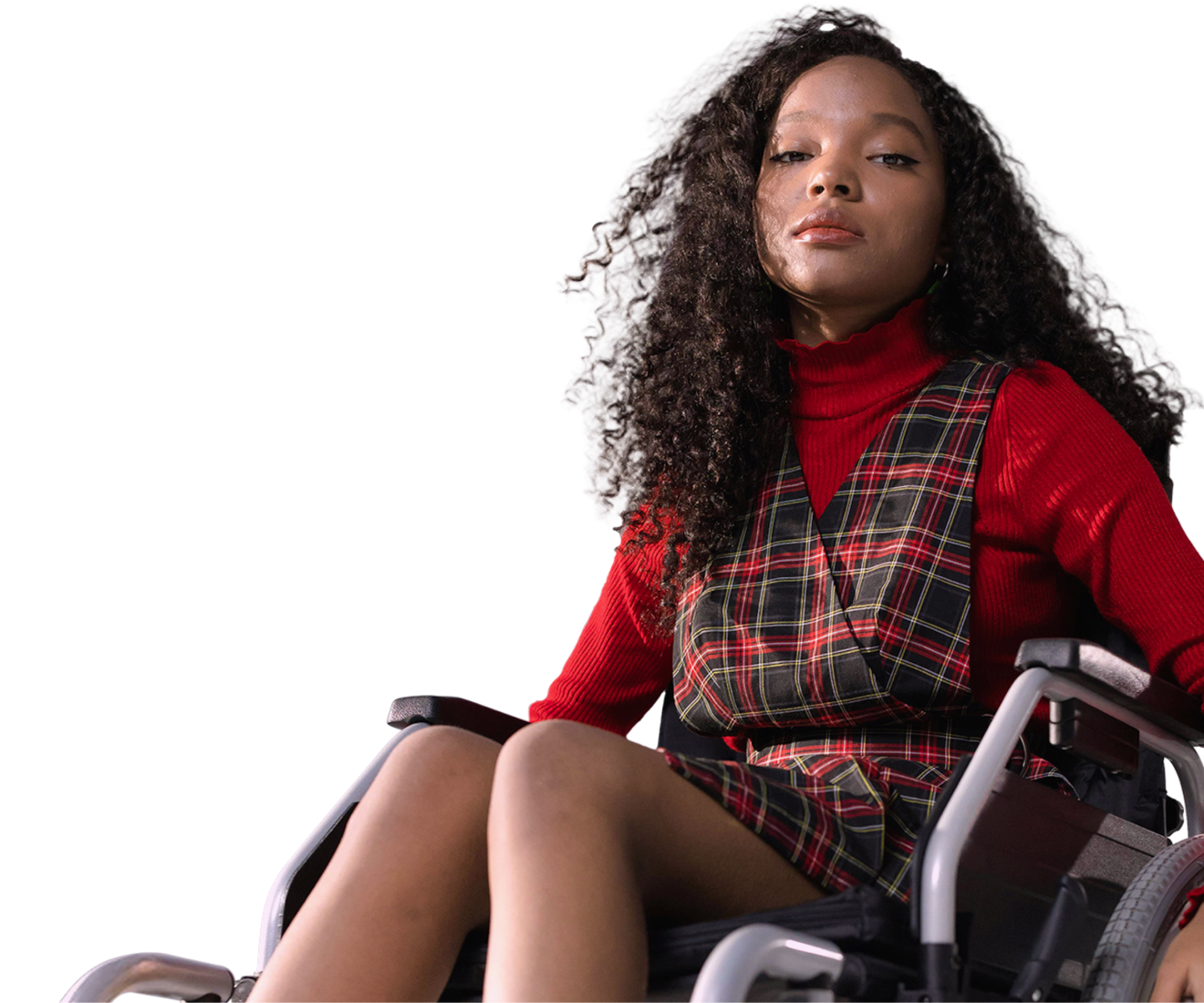 A person with brown skin and long curly dark hair sits in a manual wheelchair with their head raised proudly towards the sky. They're wearing a red long-sleeved shirt and tartan dress, in front of a faded red background, and the words "drive social change".