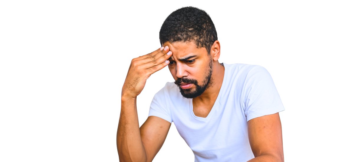 A young man with brown skin and short cropped, black hair and beard, wearing a white tee-shirt. He is leaning forward, head in hand, looking very worried.